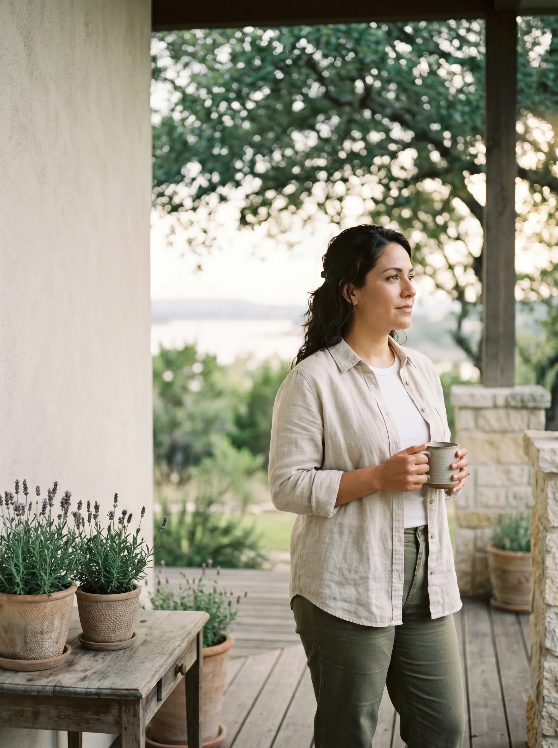 A Stepwell guest on a covered Hill Country porch at late golden afternoon, Lake Travis softly visible in the middle distance.