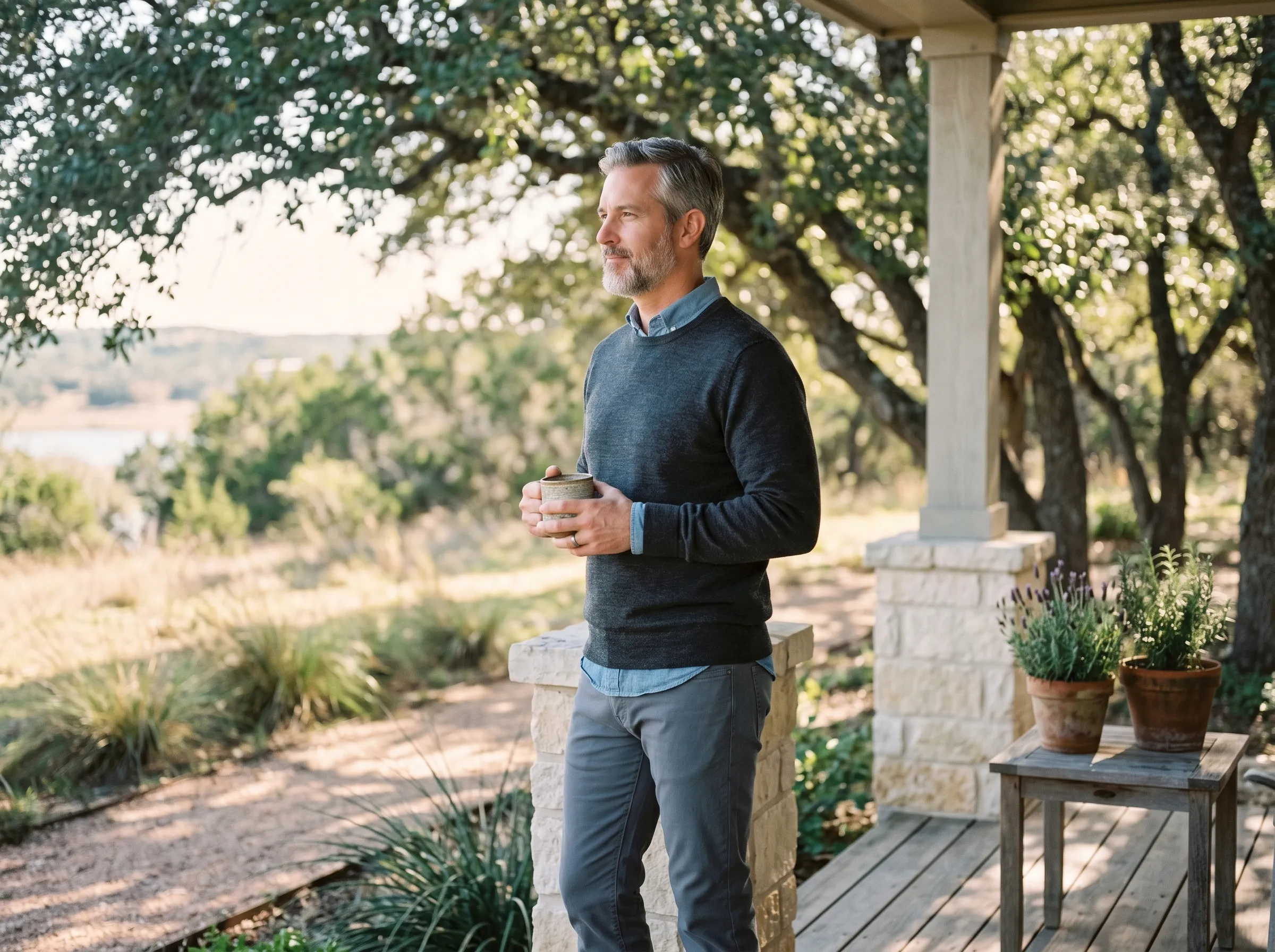 A man with coffee on a covered Hill Country porch, Lake Travis softly visible in the distance.